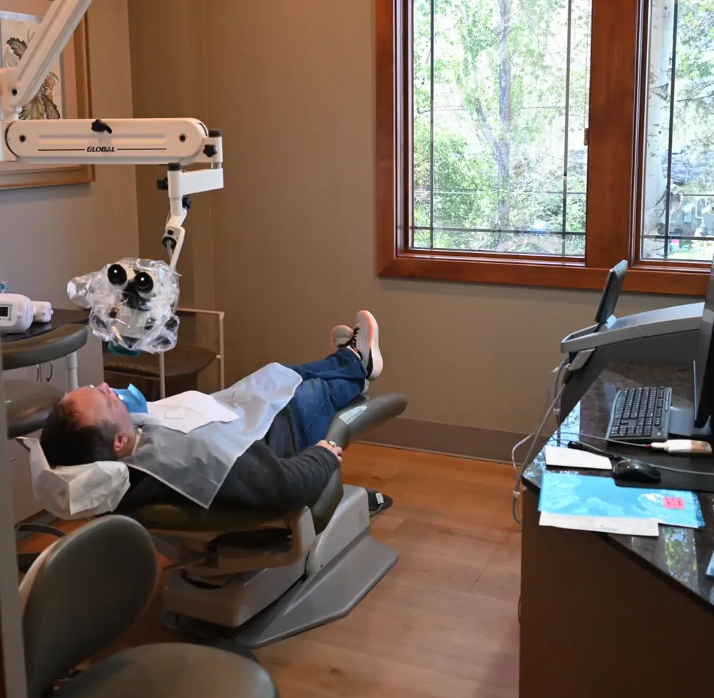 Treatment room with a patient reclined in the chair under the surgical operating microscope, beside a large window
